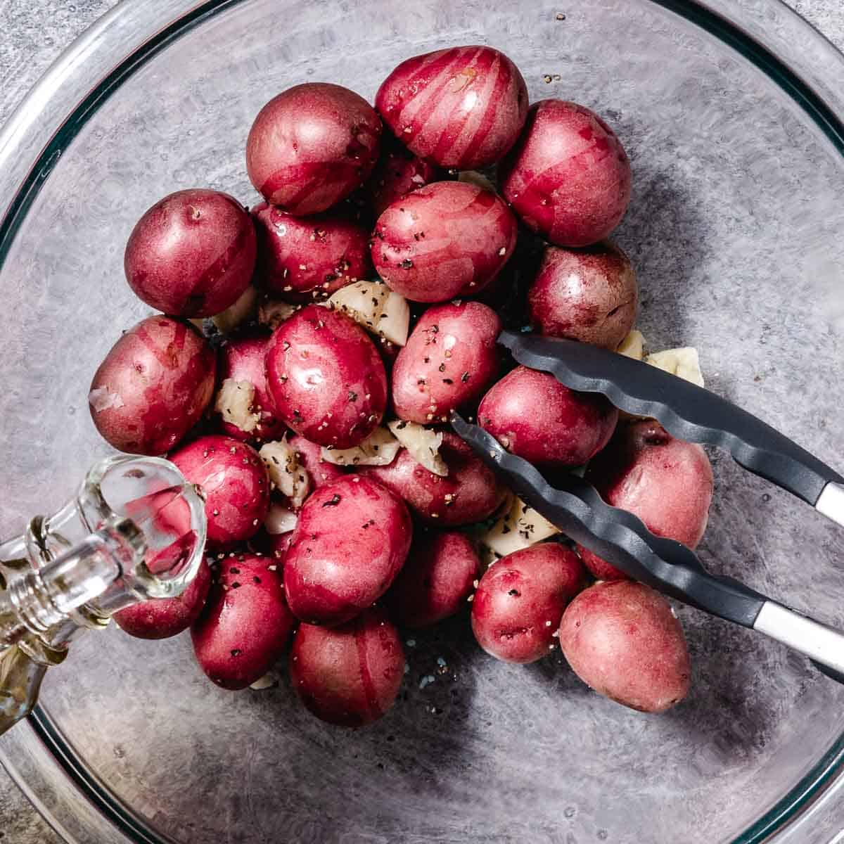 Seasoning tiny red potatoes with oil, salt, and pepper.