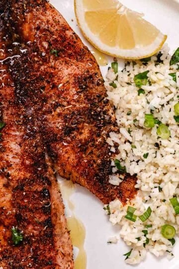 Baked red snapper fillets with lemon butter, rice, scallions, and lemon.