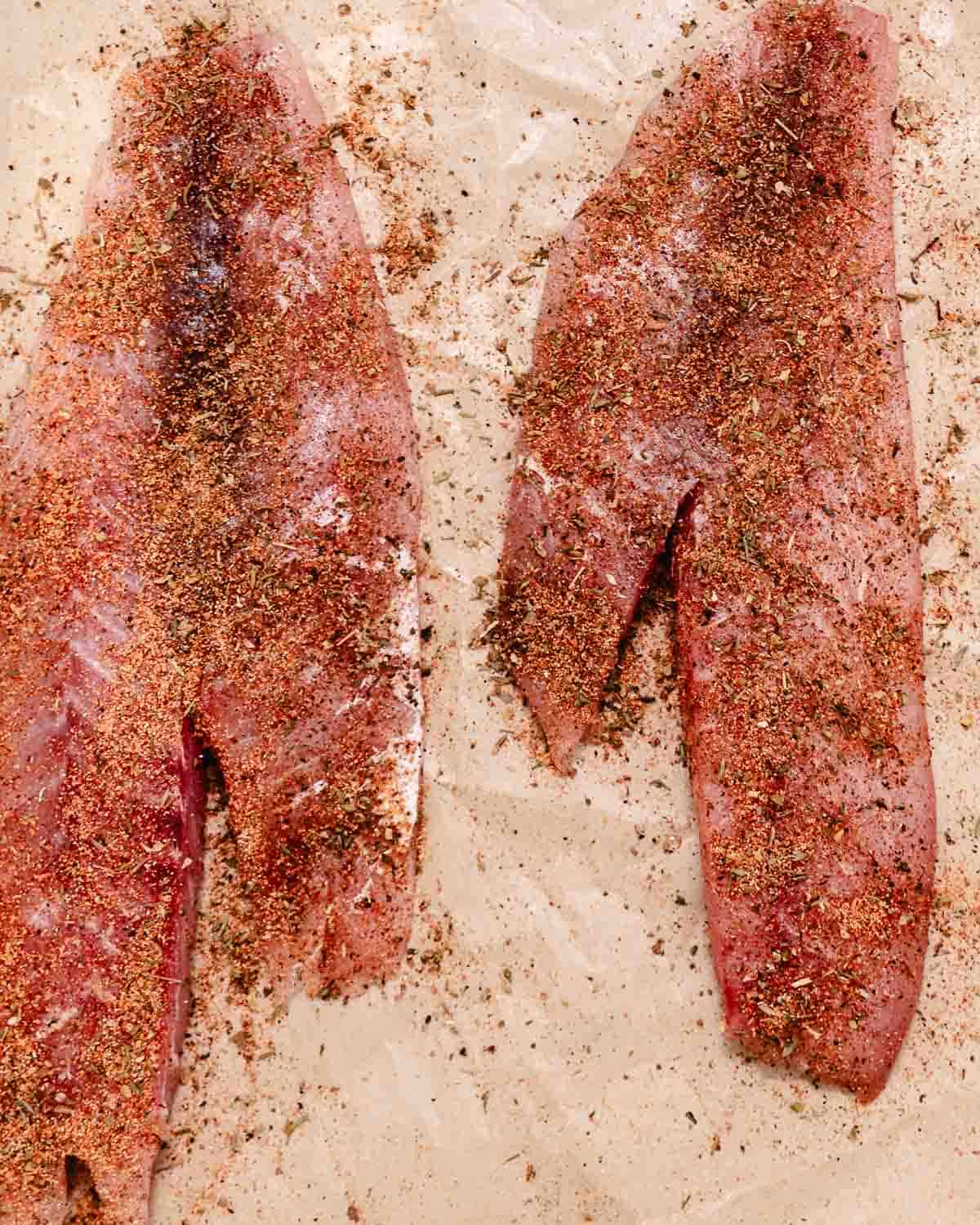 Raw red snapper fillets seasoned with blackened seasoning before baking.