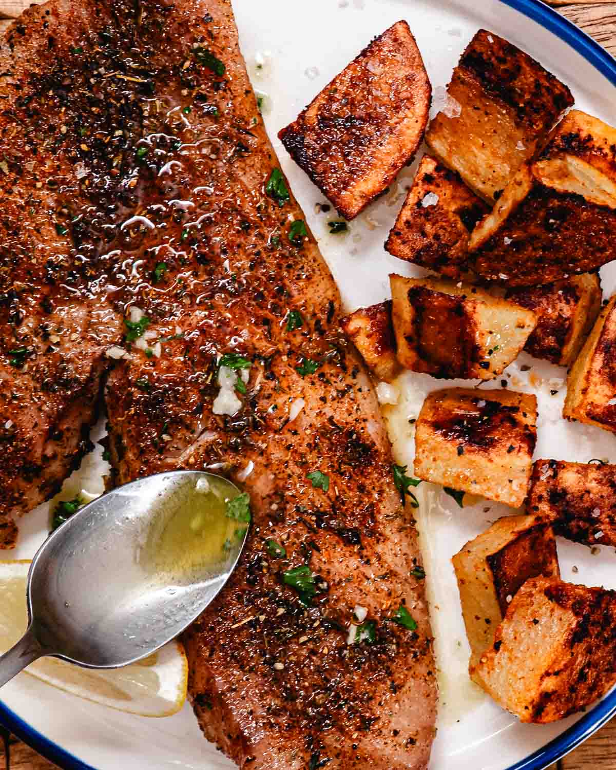 Spooning lemon butter over baked red snapper fillets with roasted potatoes.