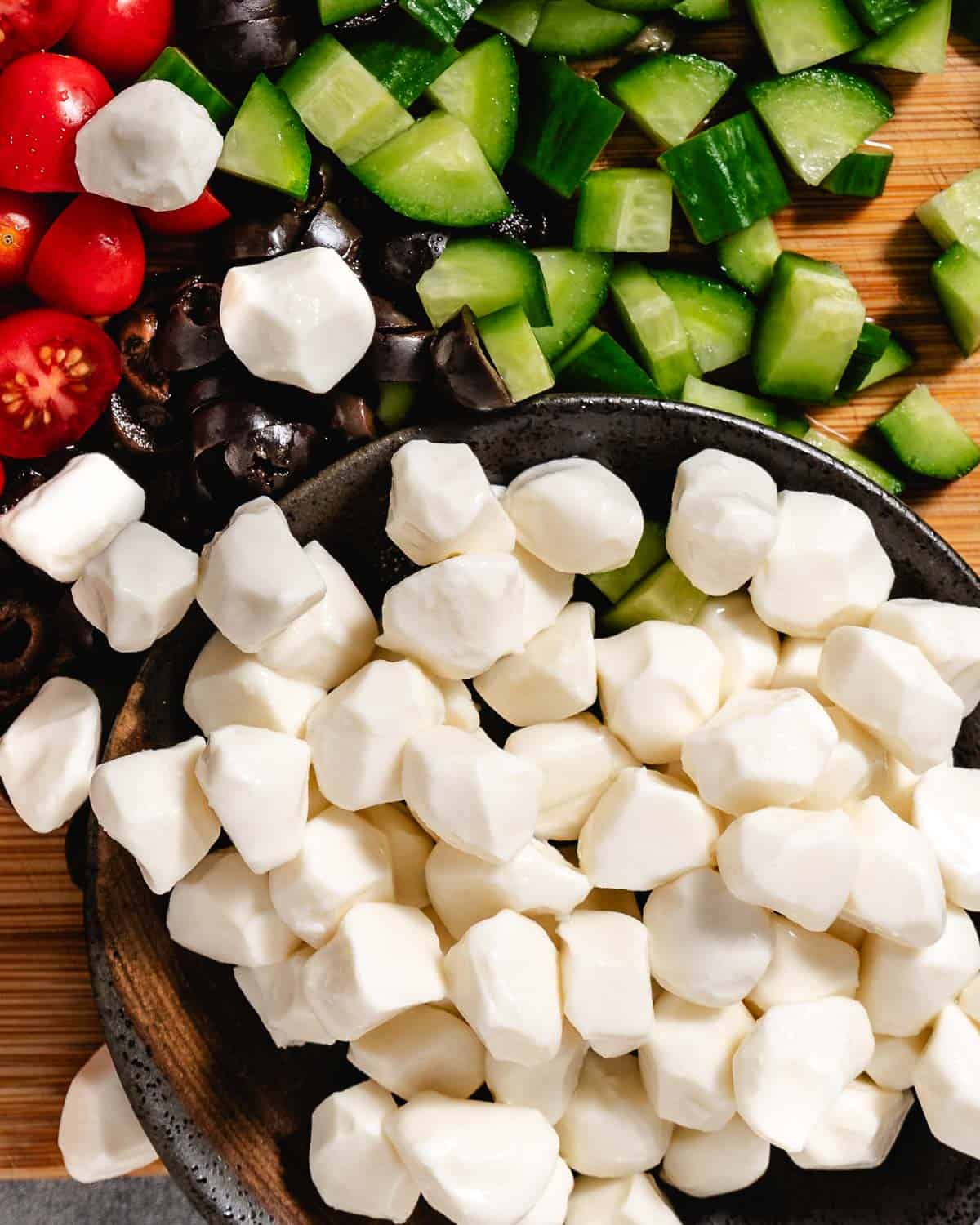 Tiny mozzarella balls with tomatoes and cucumbers in a black bowl.
