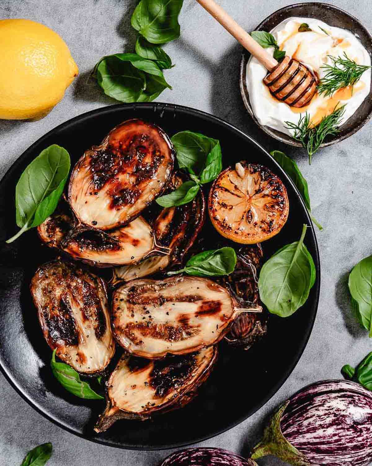 Roasted Fairy Tale eggplant with caramelized lemon, fresh basil, and a creamy yogurt dip on a black platter.