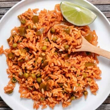 Spanish rice with peas, green bell pepper, and onion served on a white plate with a lime wedge.