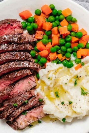 pan seared chuck steak with mashed potatoes and peas and carrots.