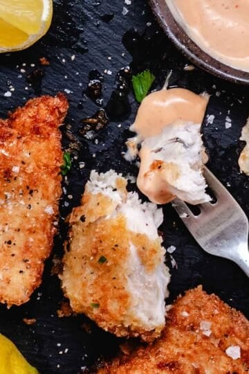 Close-up of crispy fried mahi mahi with flaky white fish inside and creamy bang bang sauce on a fork.