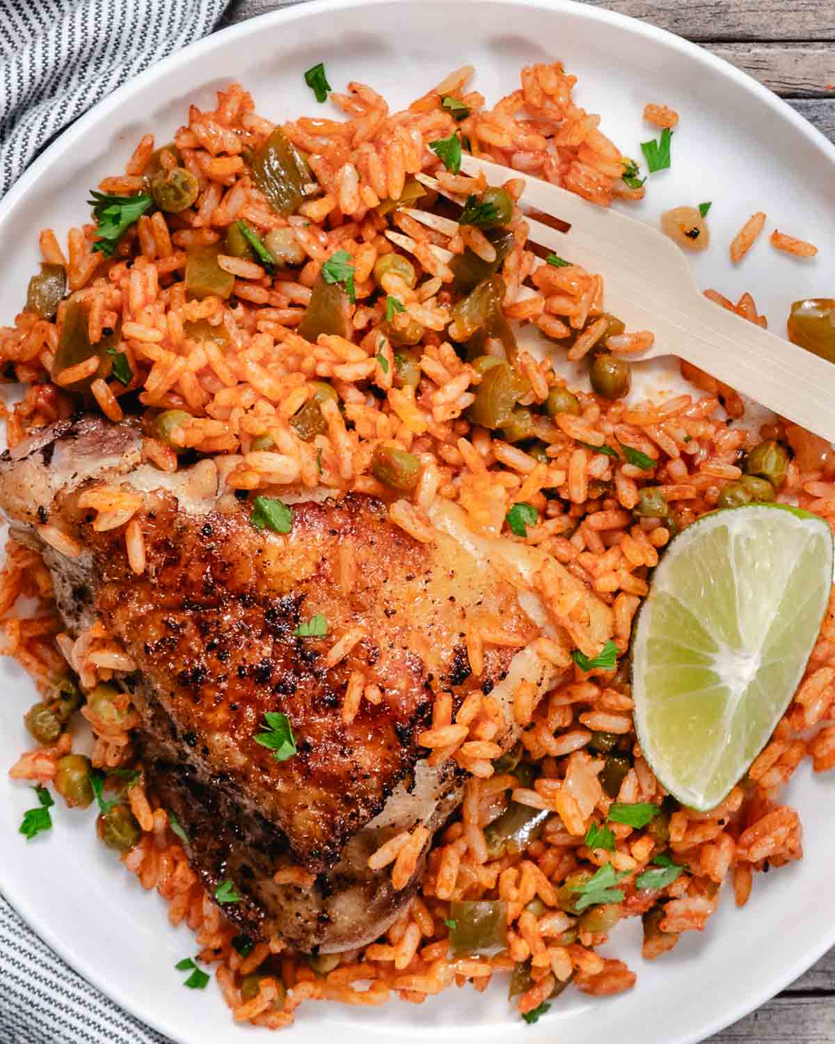 Spanish rice with peas topped with roasted chicken and lime wedges on white plate.