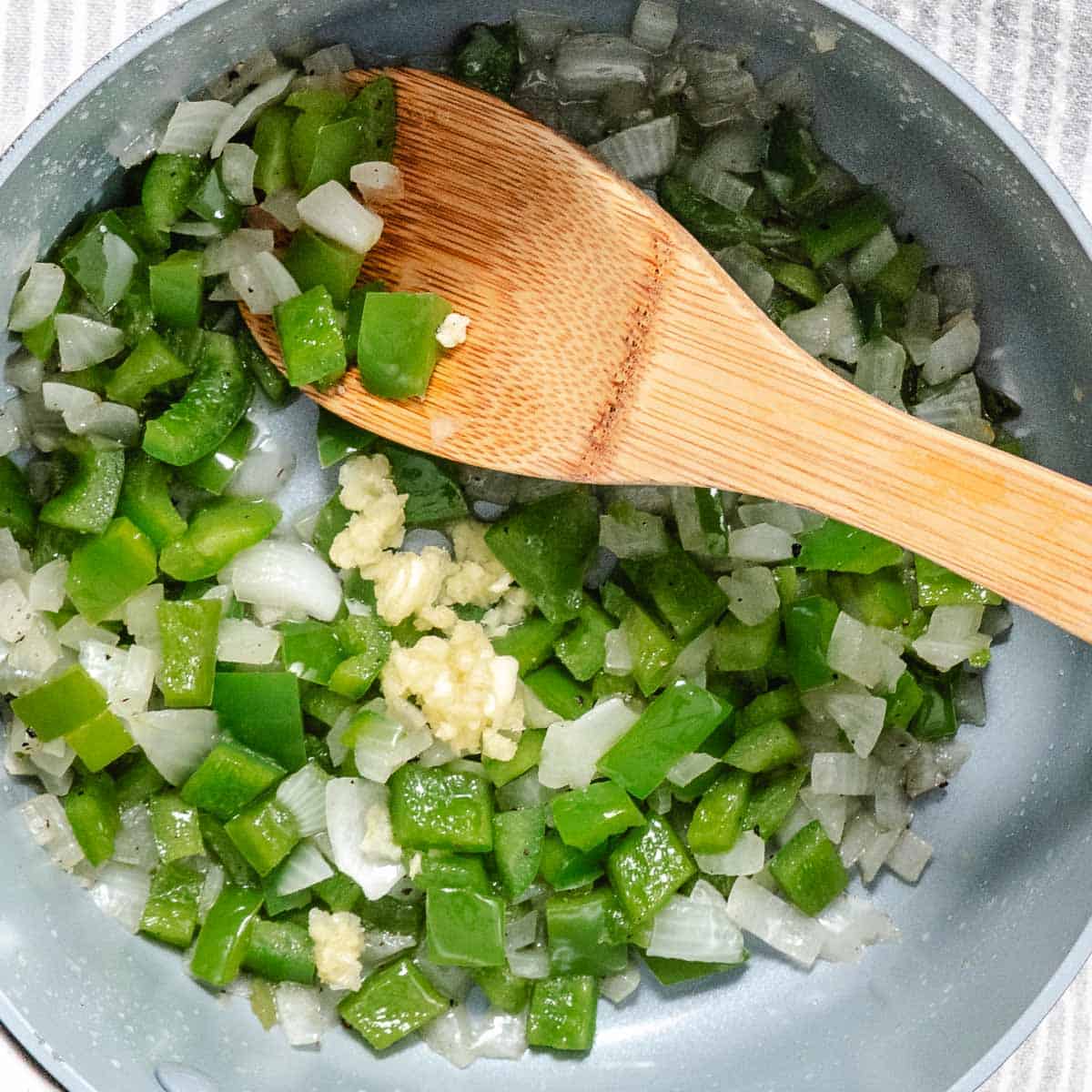 Diced green bell pepper and onion sautéing with minced garlic in a saucepan for Spanish rice.
