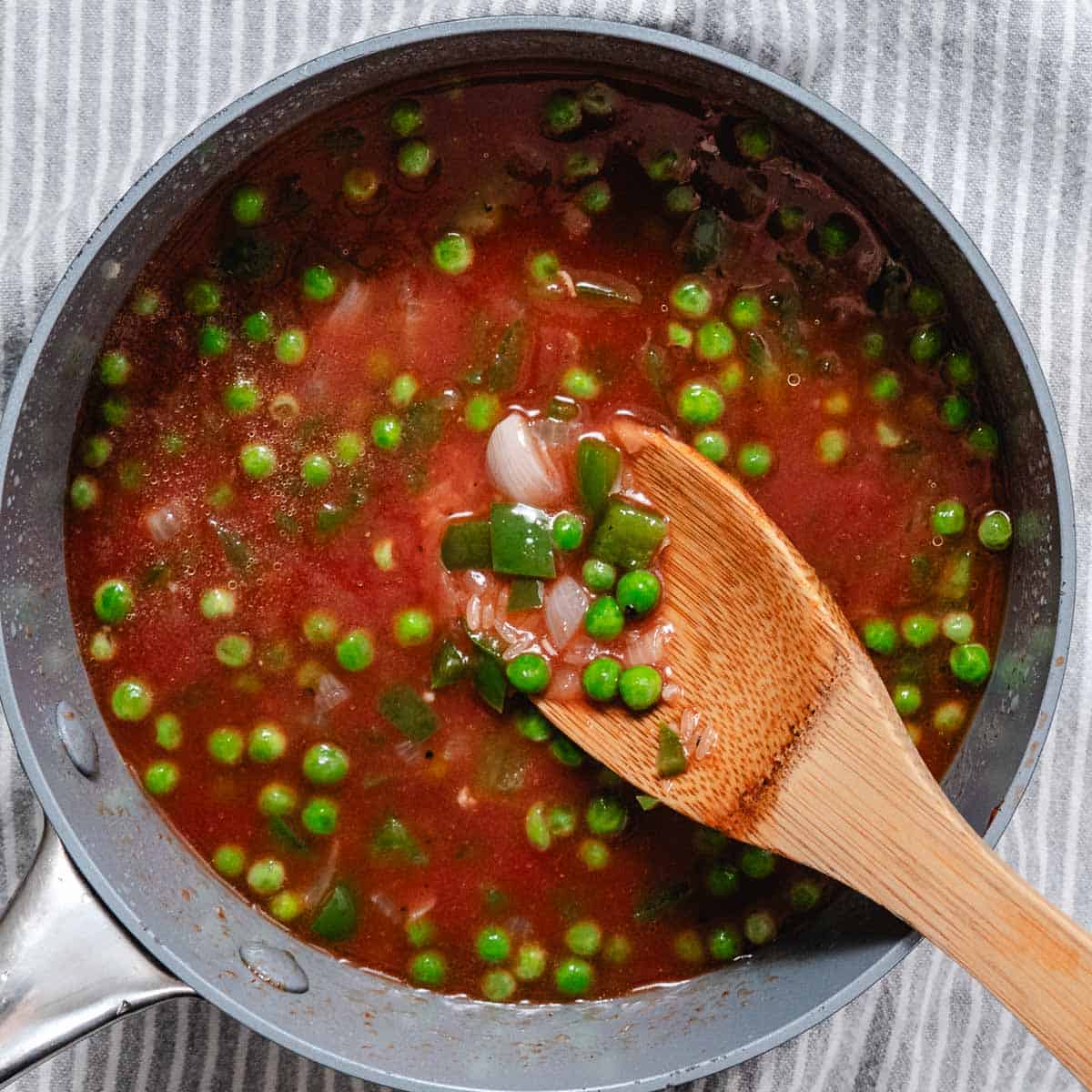 Tomato sauce, peas, onion, and green pepper simmering in a saucepan before adding the rice.