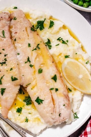white fish fillets and mashed potatoes and peas with lemon wedges on white plate