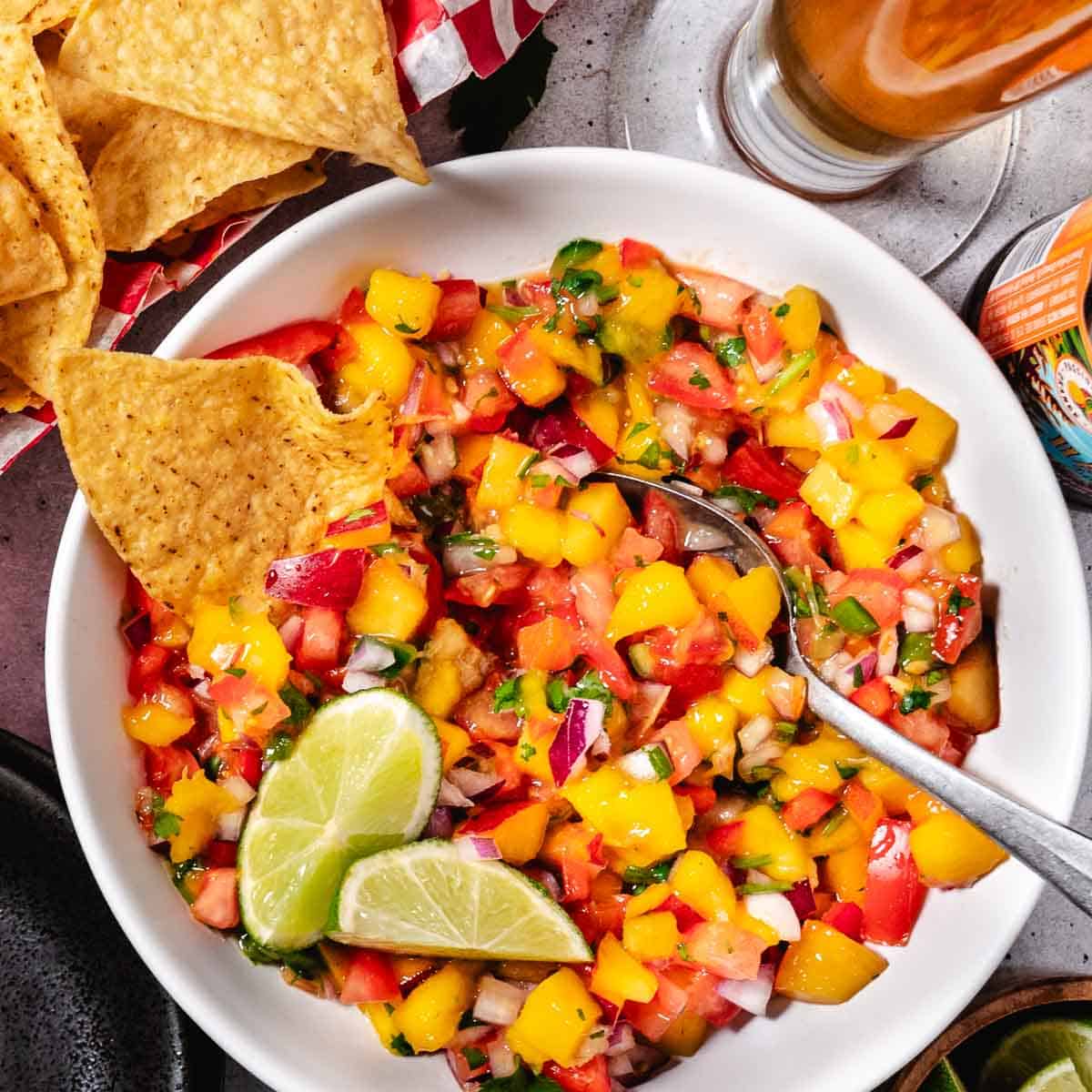 overhead view of peach mango salsa with lime and chips with a cold beer