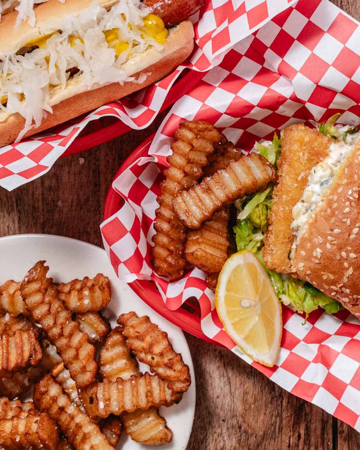 Crispy fish sandwich with homemade tartar sauce, lettuce, crinkle-cut fries, and a sauerkraut-topped hot dog.