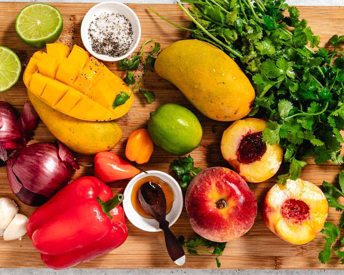 Ingredients for peach mango salsa are peaches, mangoes, habanero peppers, cilantro, onion, honey and lime.
