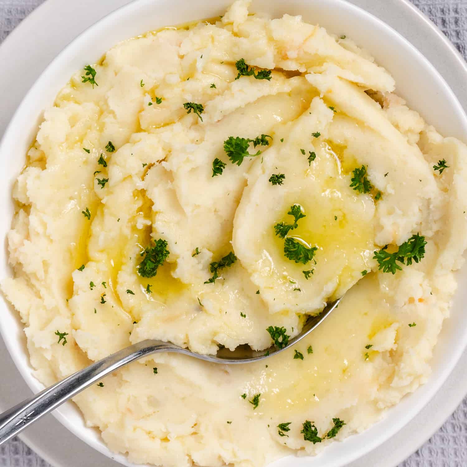 bowl of white mashed potatoes with parsley and butter.