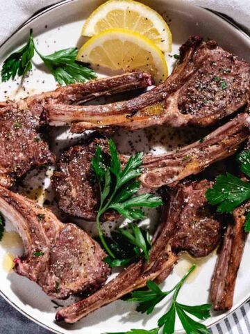 baby lambchops with lemon slices on white plate.