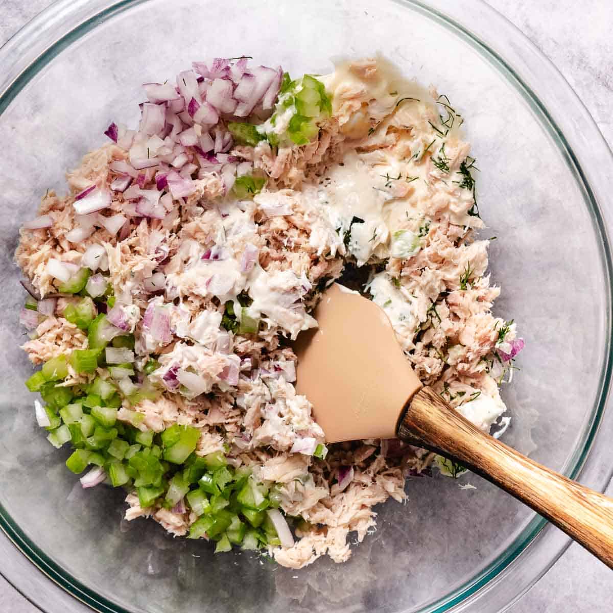 overhead view of tuna salad being mixed in a big glass bowl.