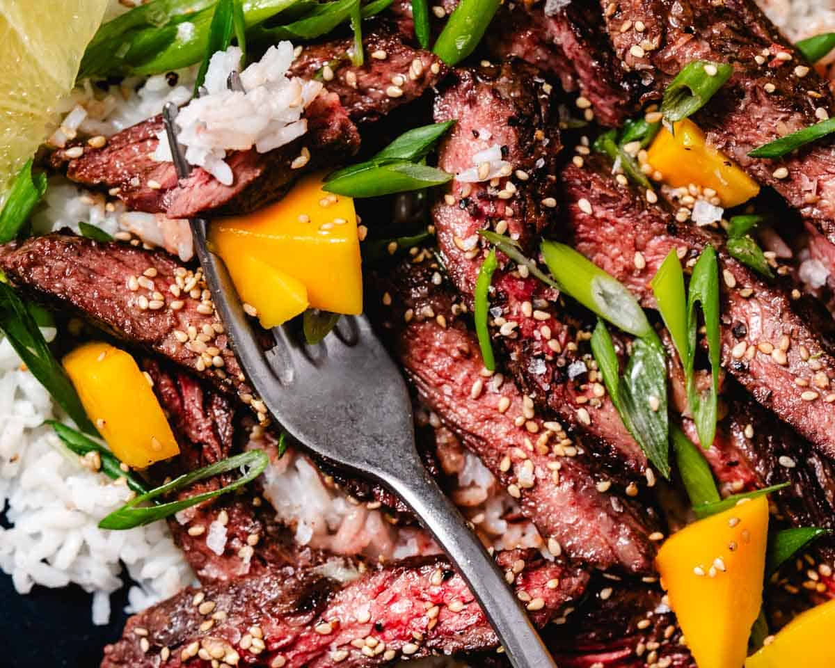 Juicy slices of cooked steak arranged on a plate, served over rice with mango