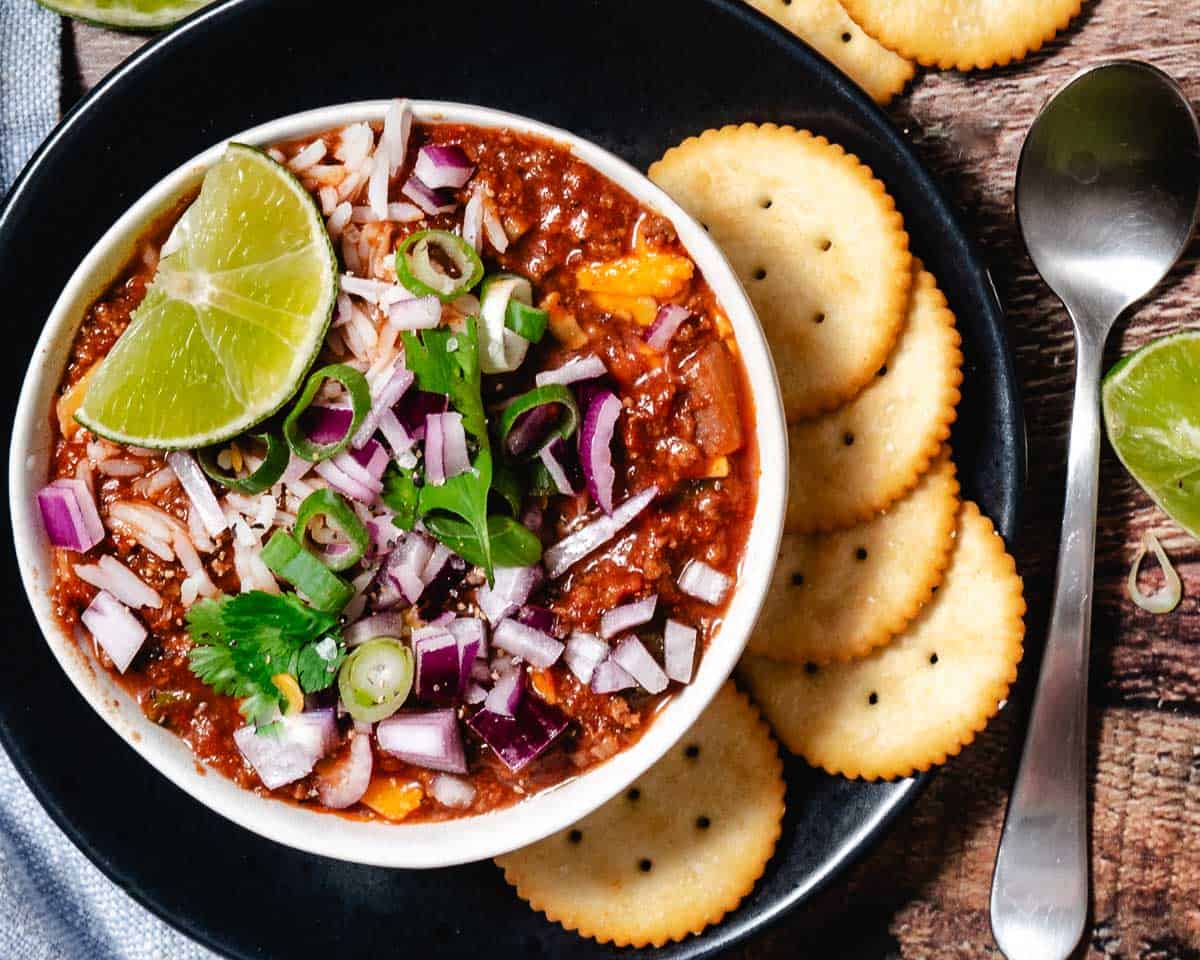 bowl of hot chili with cheese, parsley, onions, and crackers