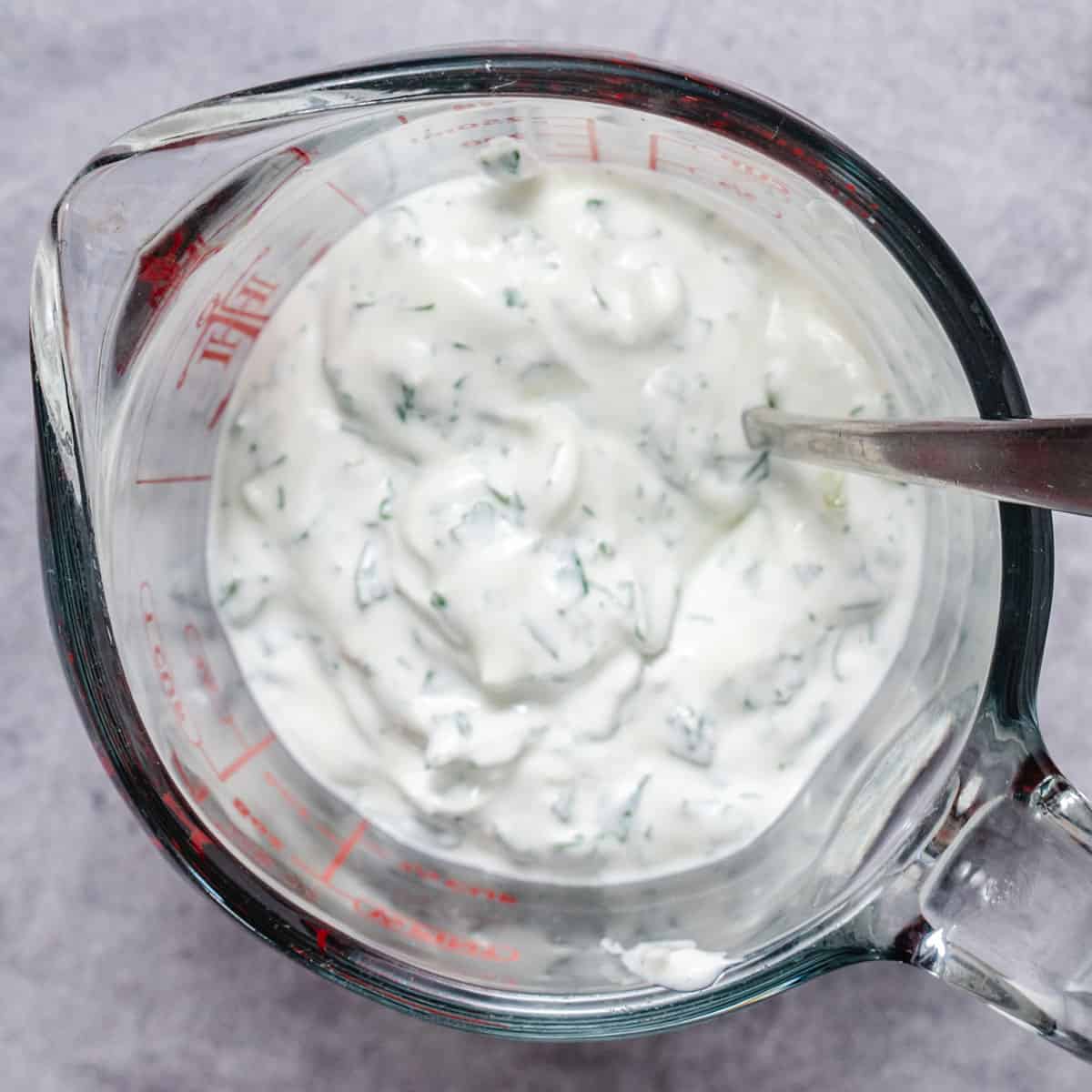 cilantro lime crema in glass measuring cup with fresh cilantro and lime