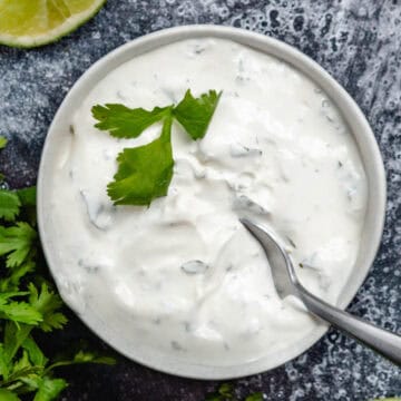 cilantro lime crema in white bowl with fresh cilantro and lime