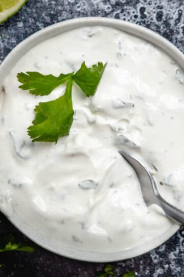 cilantro lime crema in white bowl with fresh cilantro and lime