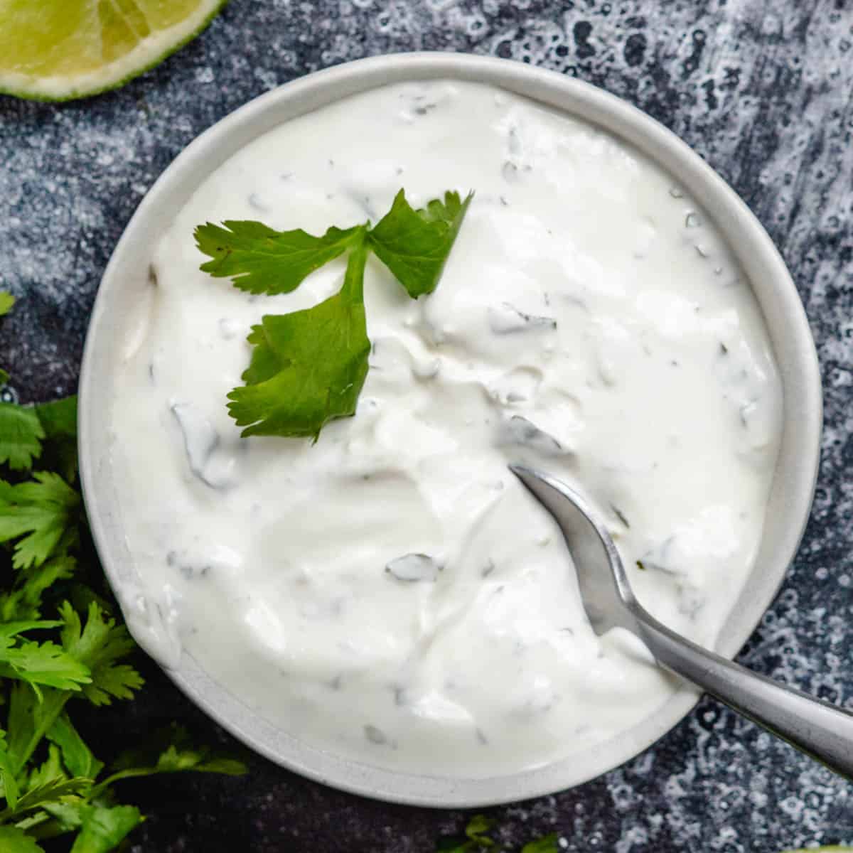 cilantro lime crema in white bowl with fresh cilantro and lime
