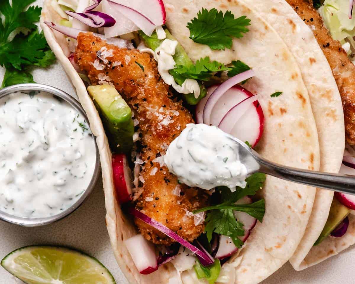 cilantro lime crema spooned over crispy tacos with cabbage and lime
