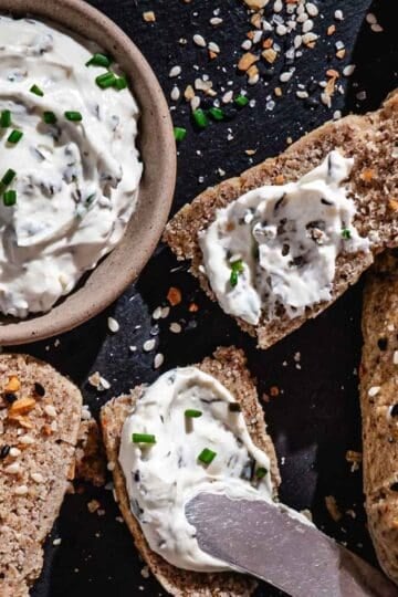 Gluten-free everything bagel breadsticks served with chive cream cheese on a dark platter.