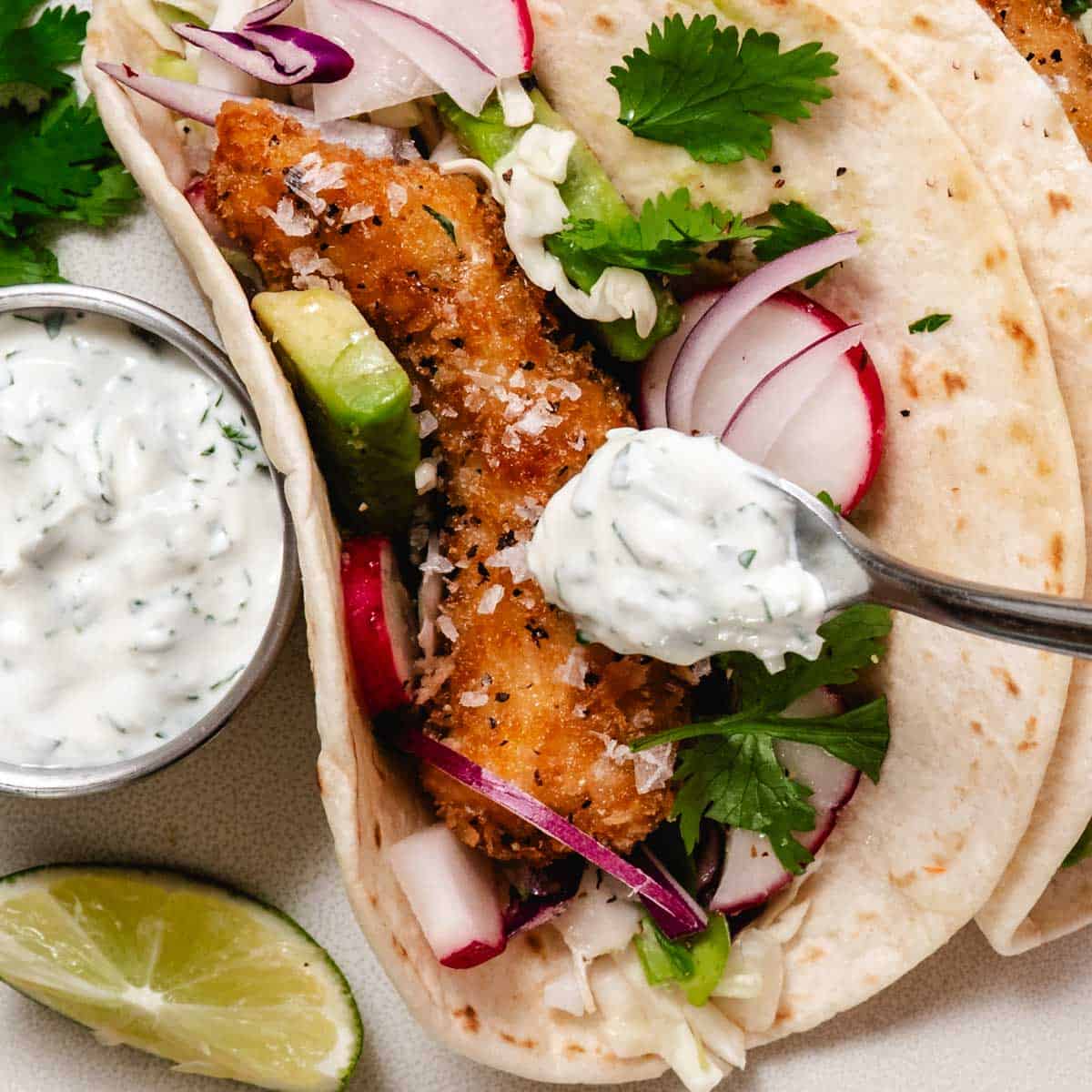 cilantro lime crema spooned over fish tacos with cabbage and lime