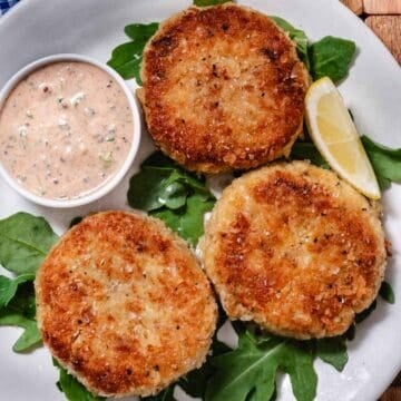 Three golden crab cakes with claw meat, remoulade sauce, and a lemon wedge.