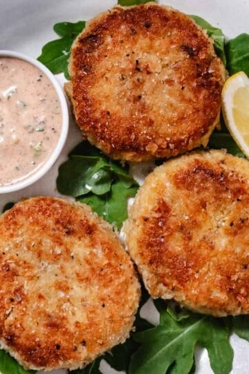 Three golden crab cakes with claw meat, remoulade sauce, and a lemon wedge.