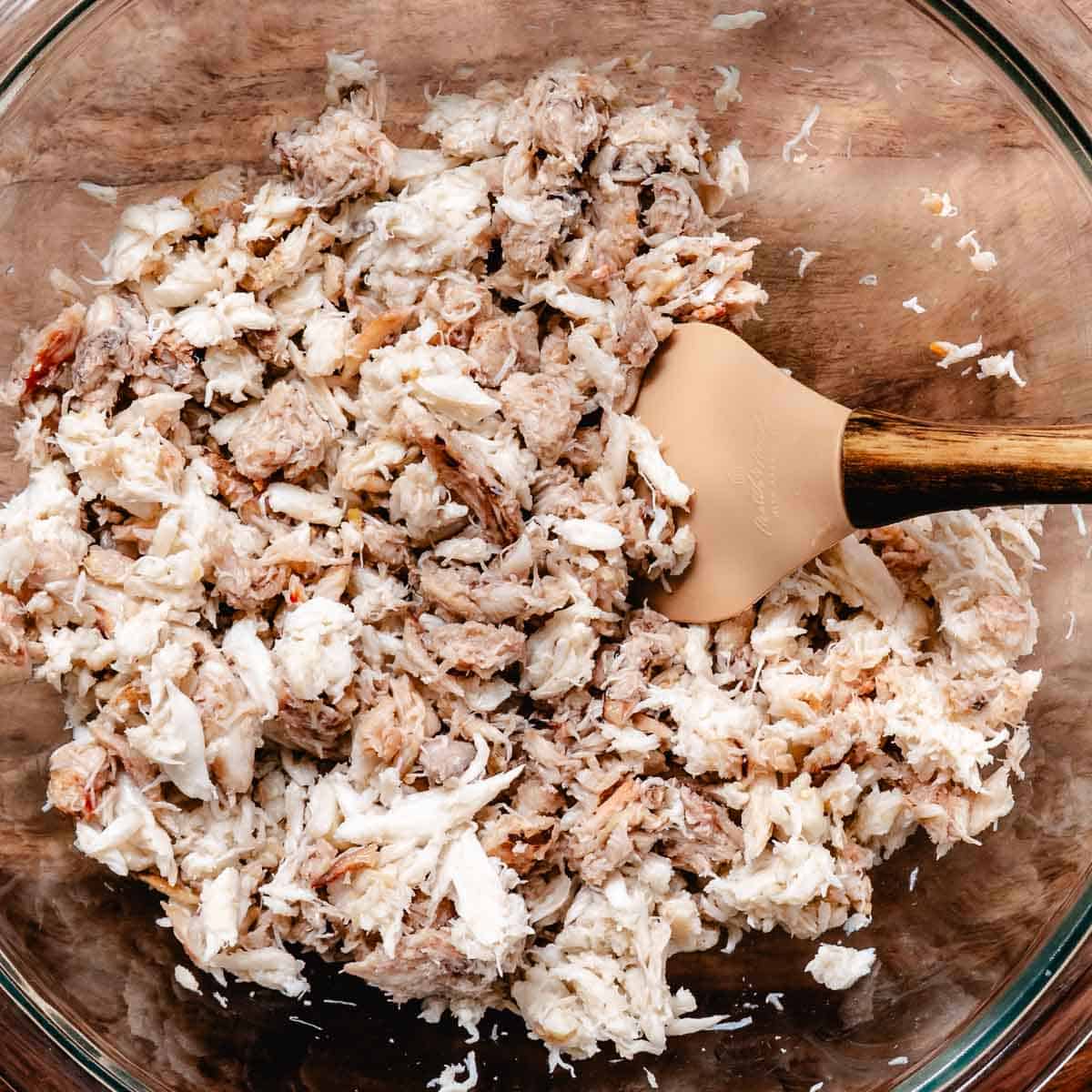 Lump and claw crabmeat being gently mixed in a glass bowl.