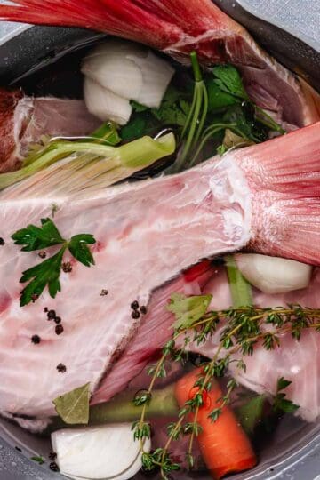 Red snapper bones with vegetables and herbs in a pot for homemade fish stock.