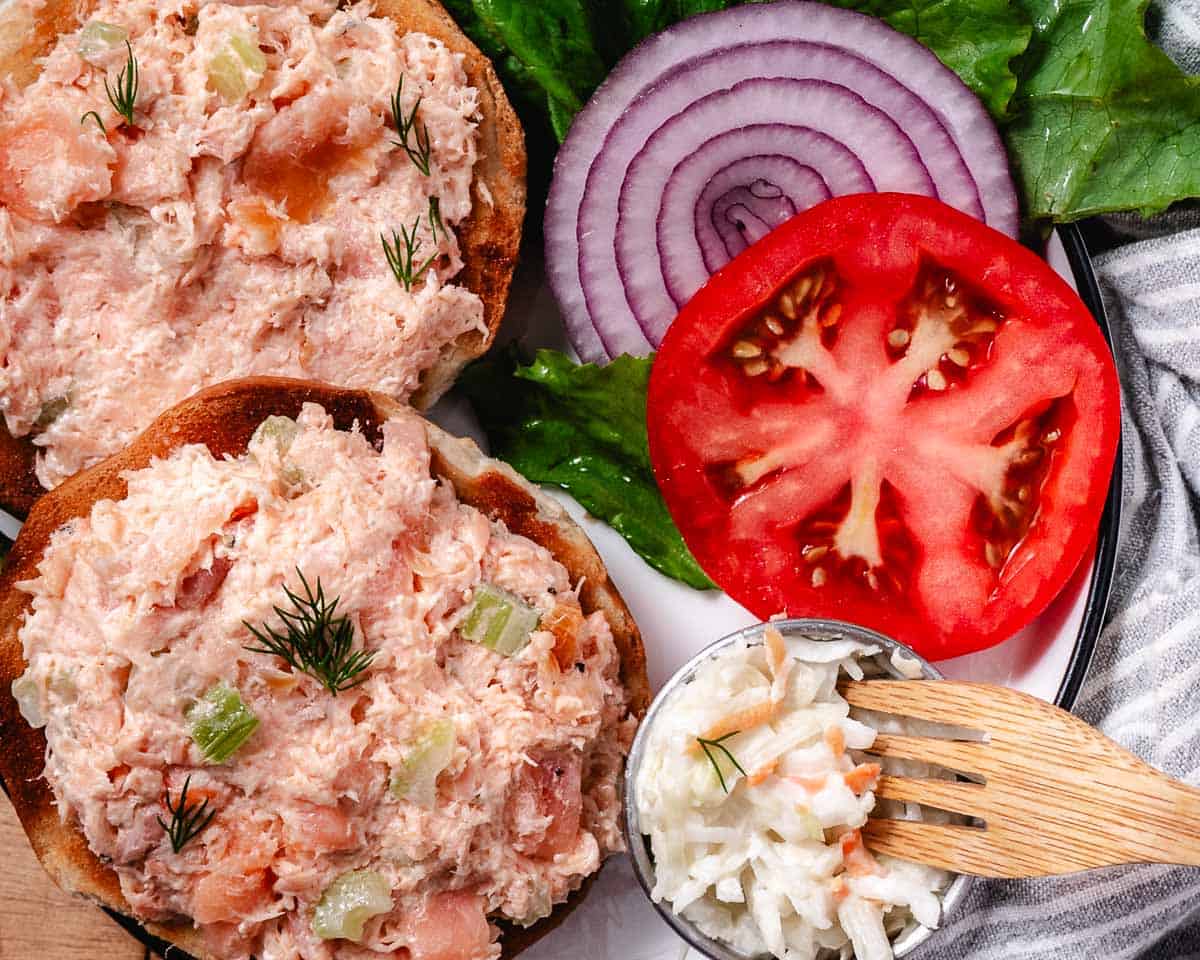 baked salmon salad in a bagel with lettuce, onions, and tomato slices