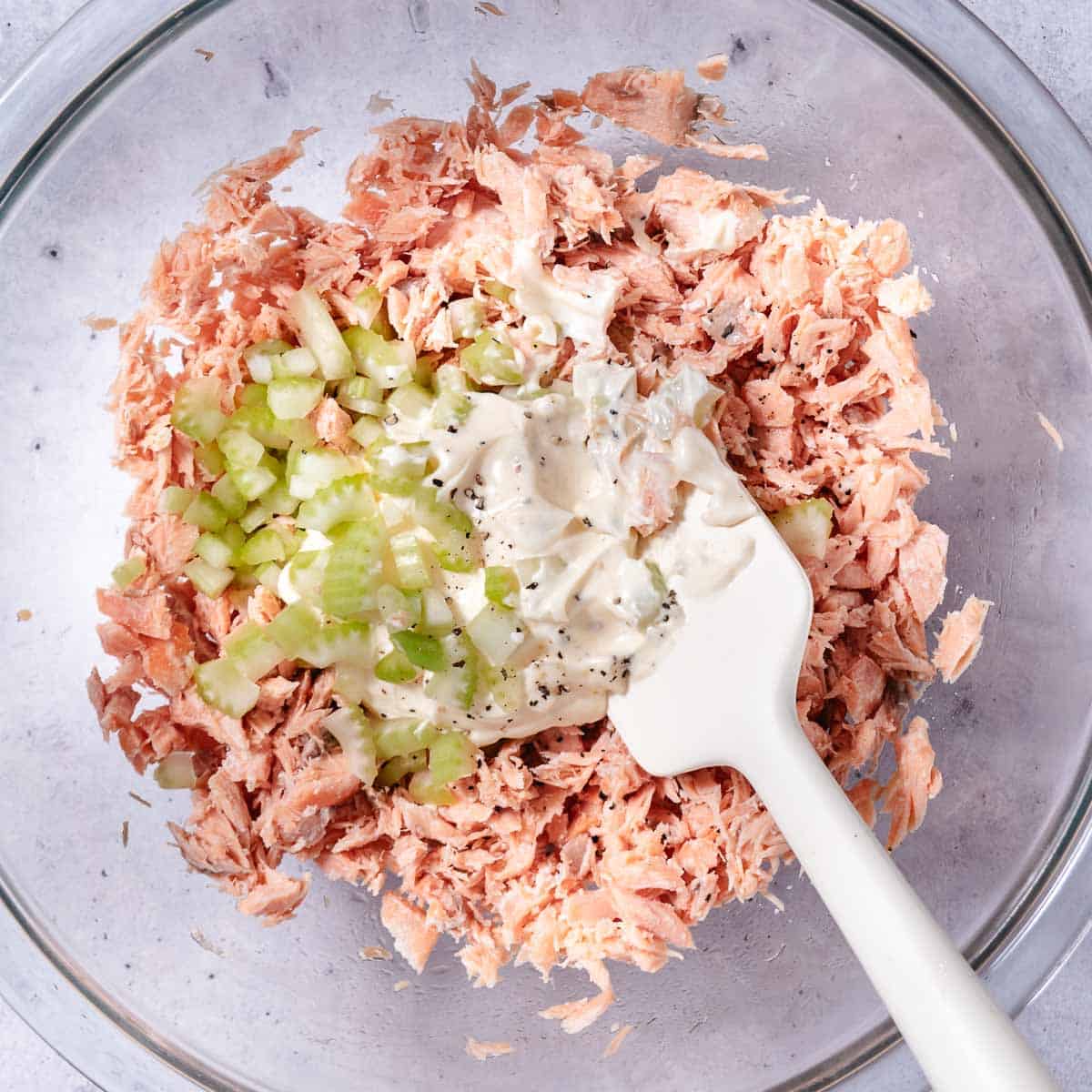 Baked salmon flaked in a bowl with mayonnaise, celery, lemon juice, and onion powder for salmon salad.