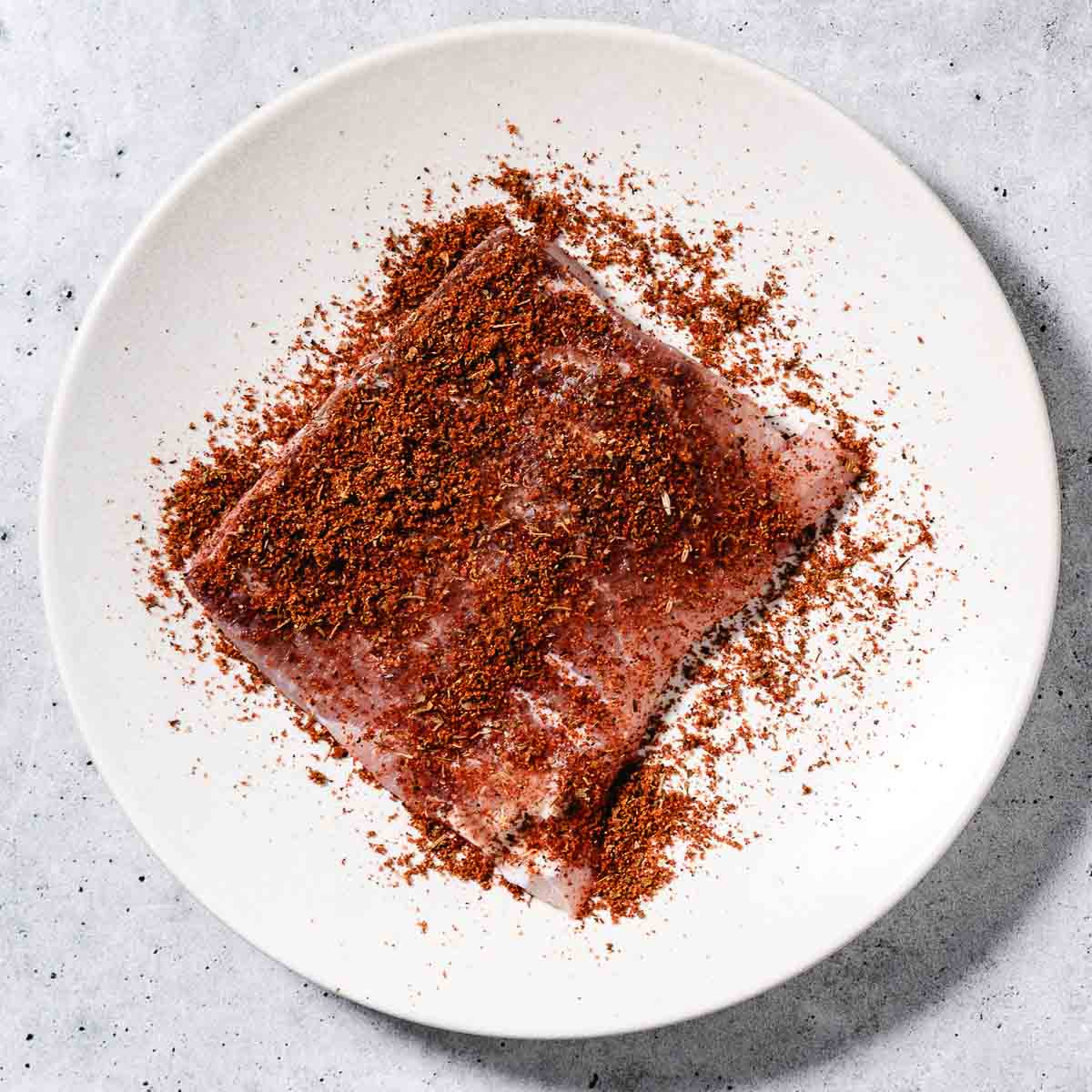 tripletail filet with blackened seasoning on a plate before cooking