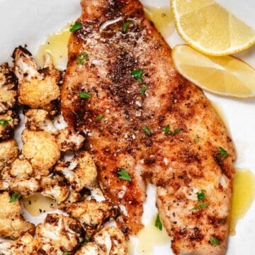 Yellowtail snapper on white plate with cauliflower and lemon.