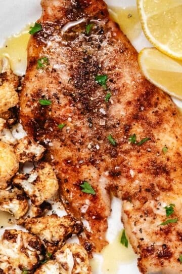 Yellowtail snapper on white plate with cauliflower and lemon.