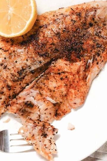 Broiled yellowtail snapper with lemon on white plate.
