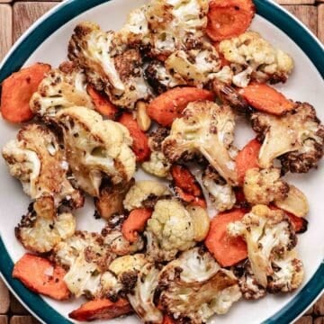 Roasted cauliflower, carrots, and garlic on a plate.