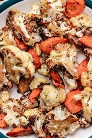Roasted cauliflower, carrots, and garlic on a plate.