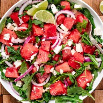 Fresh watermelon arugula salad with feta and red onion on a serving platter, topped with lime vinaigrette.