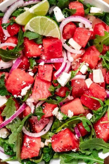 Fresh watermelon arugula salad with feta and red onion on a serving platter, topped with lime vinaigrette.