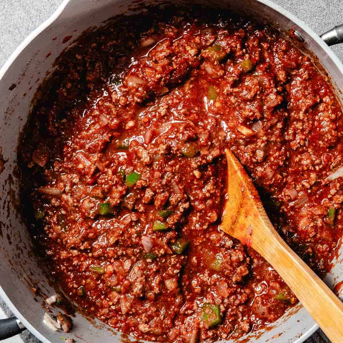 Thick chuck steak chili simmering in a pot with a wooden spoon.