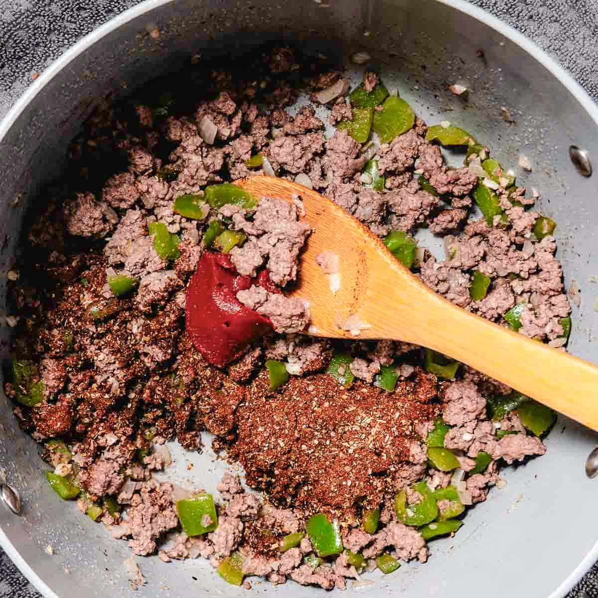 Tomato paste and chili spices added to browned ground chuck and vegetables.