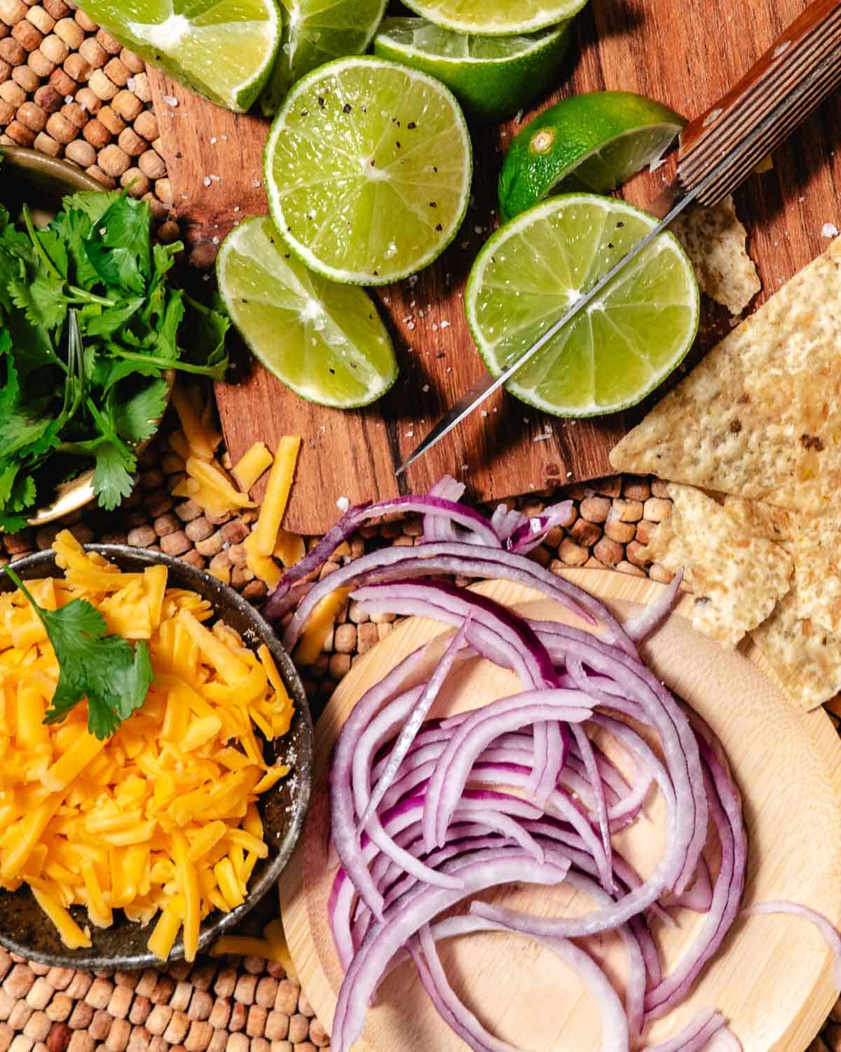 Shredded cheddar, sliced red onion, cilantro, lime wedges, and tortilla chips for topping chili.