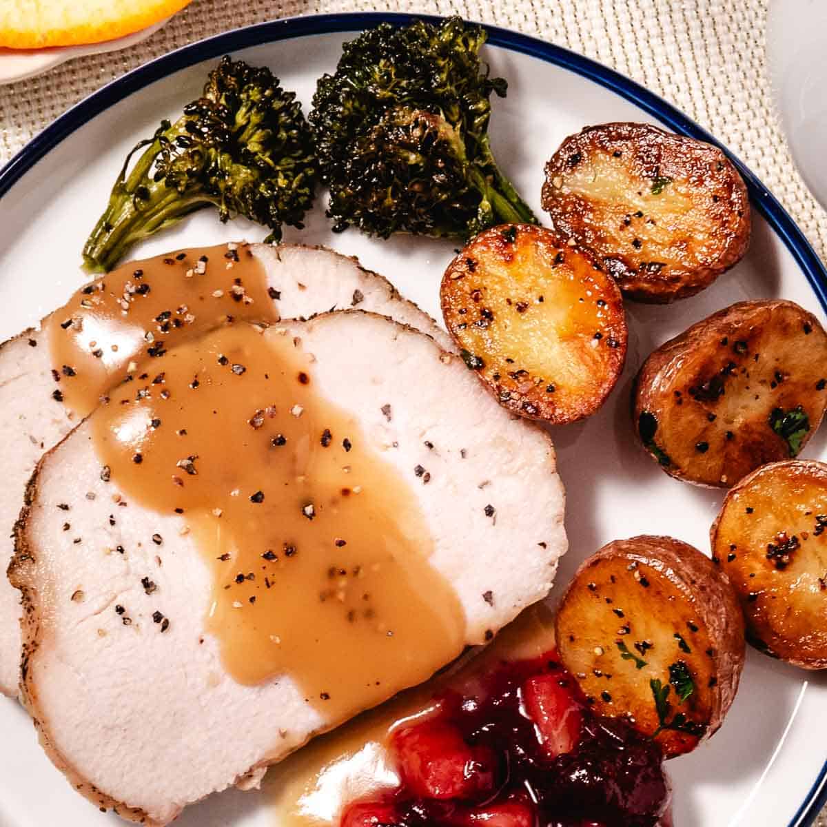 Roasted Butterball turkey breast sliced on a plate with gravy, cranberry sauce, potatoes and broccoli.