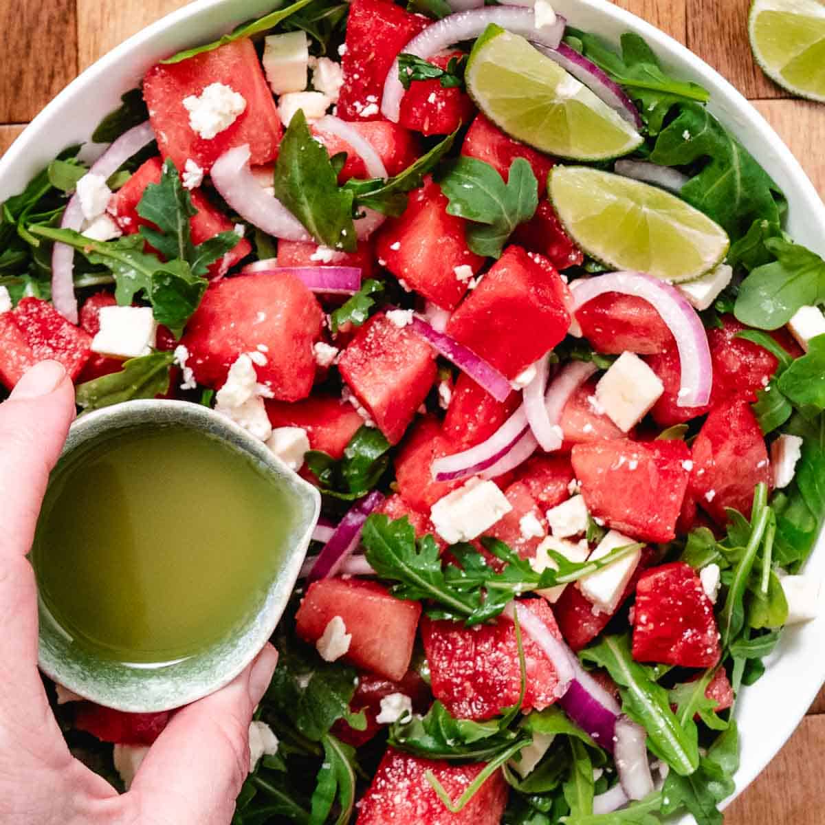 Pouring lime vinaigrette over watermelon arugula salad.