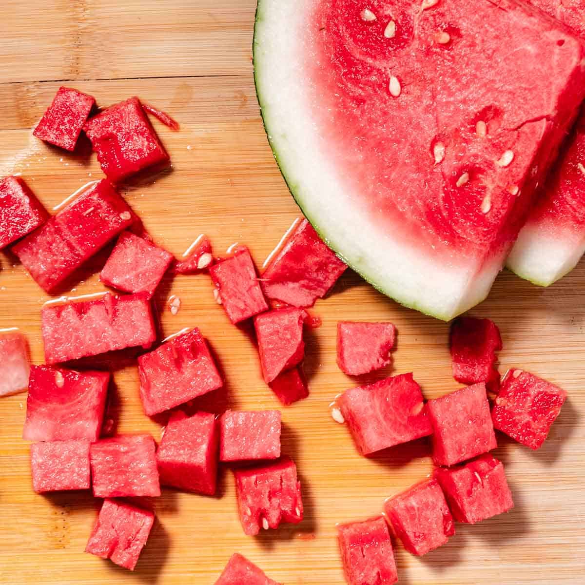 Fresh watermelon wedges and cubes on a wooden cutting board .