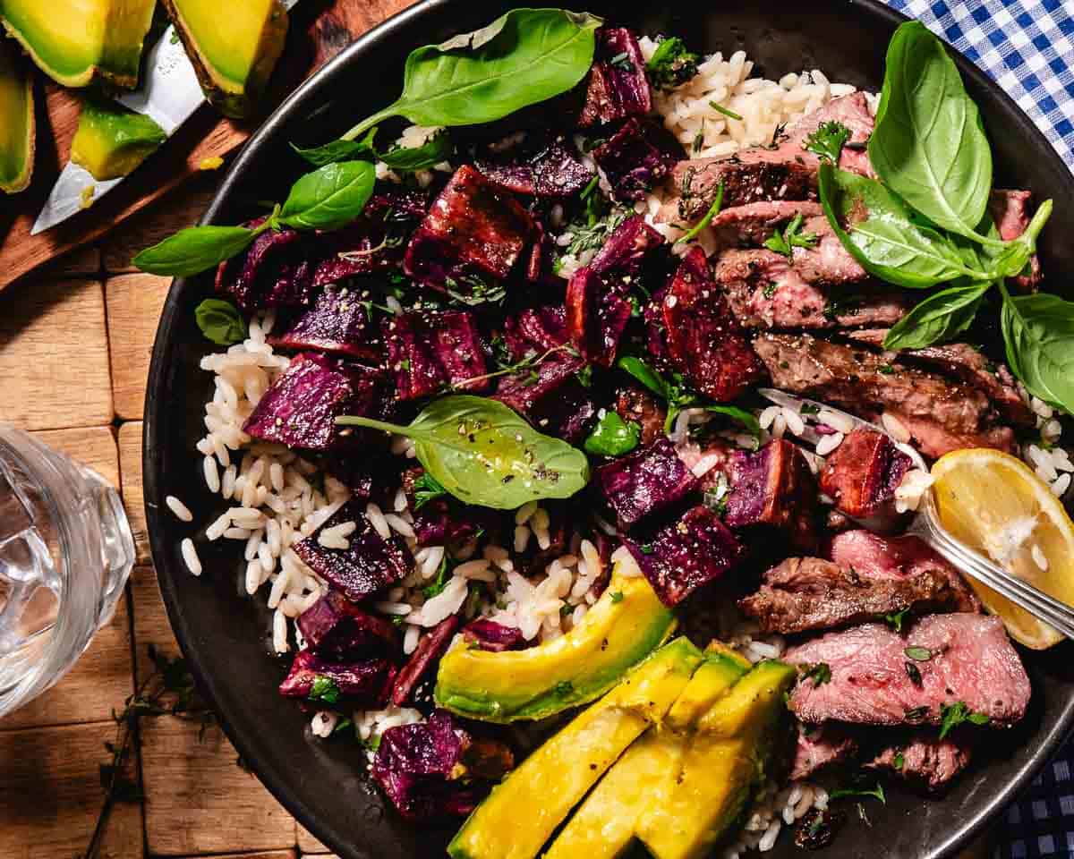 purple potatoes with seared steak, avocado, basil and rice in a bowl.