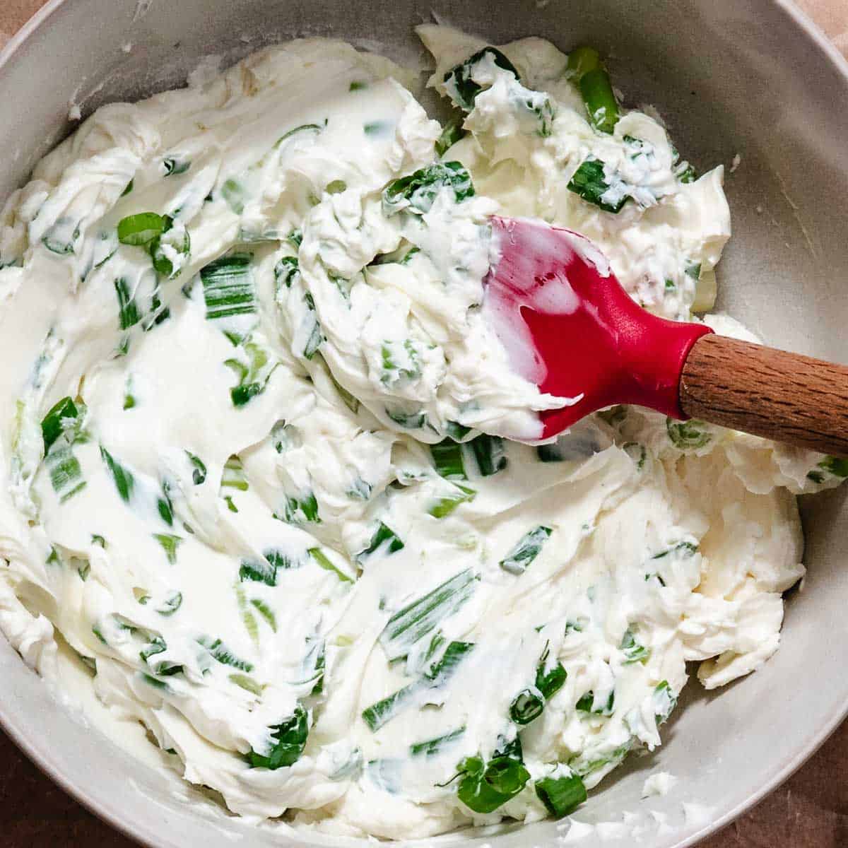 mixing bowl with scallions and cream cheese with a rubber spatula.